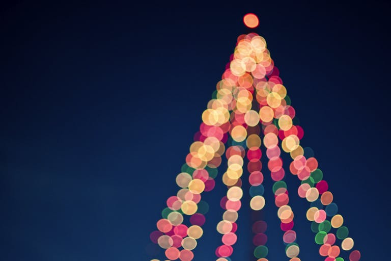 Colorful bokeh lights forming a Christmas tree against a dark blue sky.